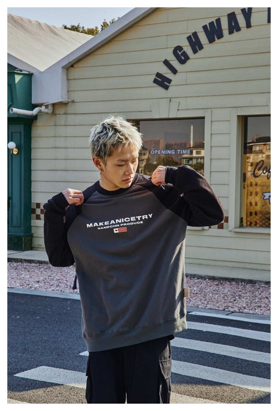 Model holding out a charcoal sweatshirt with black sleeves and a white chest graphic, shown from the front.