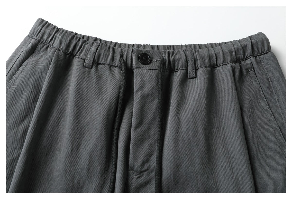 Close-up of charcoal gray pants showing the elastic waistband, button closure, belt loops, and front pockets.