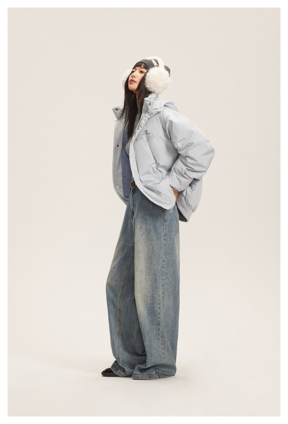 Model wearing a pale blue hooded padded jacket with oversized jeans and furry earmuffs.
