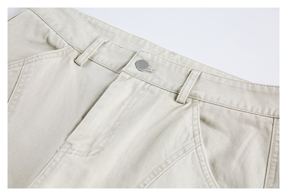 Close-up of light beige trousers showing the waistband, metal button, belt loops and front pocket.