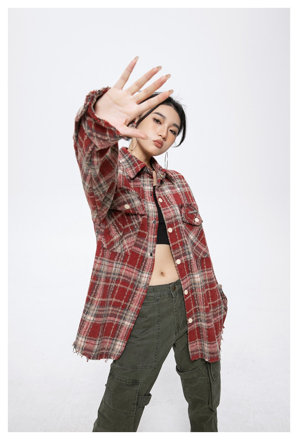 Model wearing the red plaid shirt-jacket open, with one hand raised toward the camera, with green cargo pants