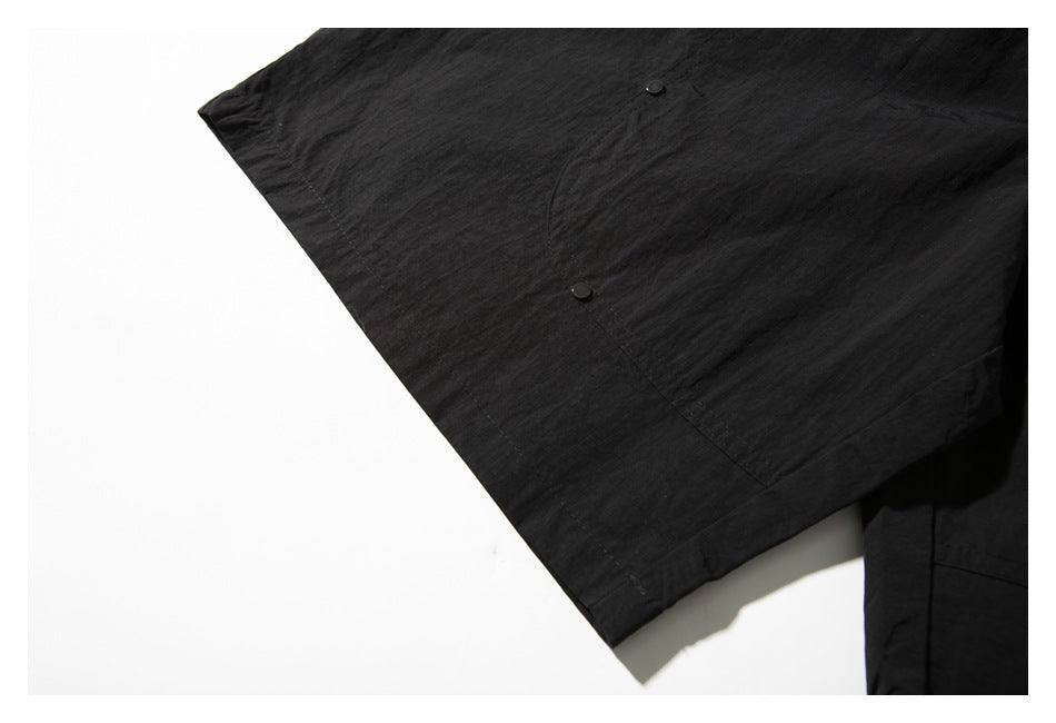 Close-up of a black garment showing a large stitched pocket with two black snaps.