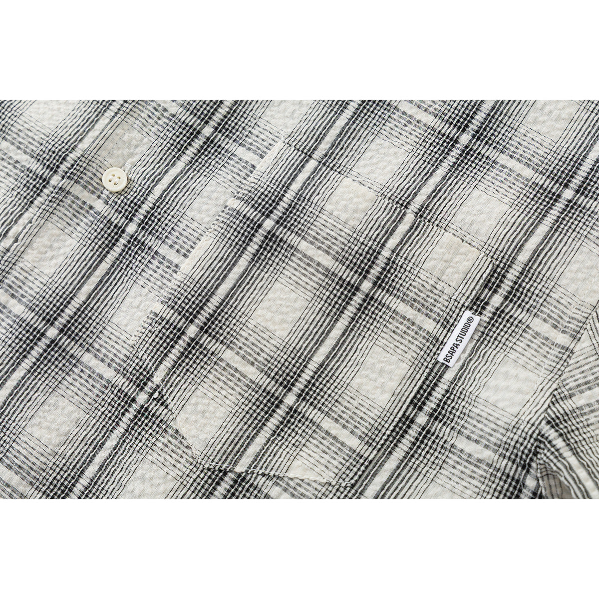 Close-up of cream and black plaid fabric, a button, and a small sewn label.