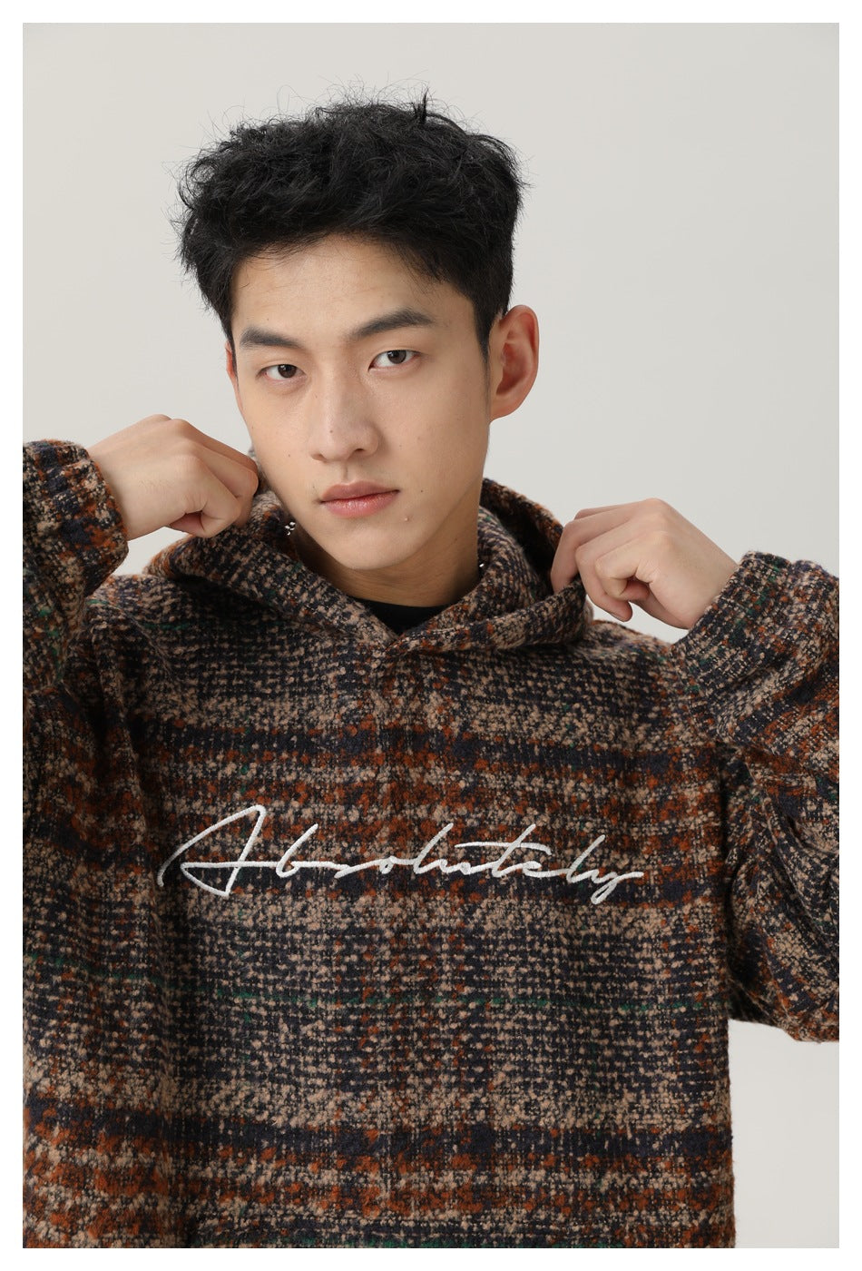 Model wearing a brown, charcoal, and cream plaid hooded pullover with white script across the chest.