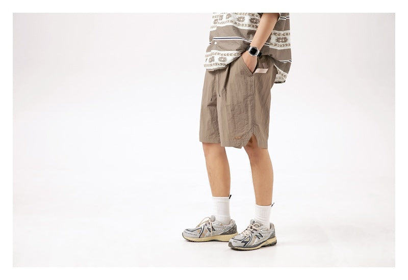 Side view of a model wearing taupe knee-length shorts with an elastic waist, pockets, and side slit.