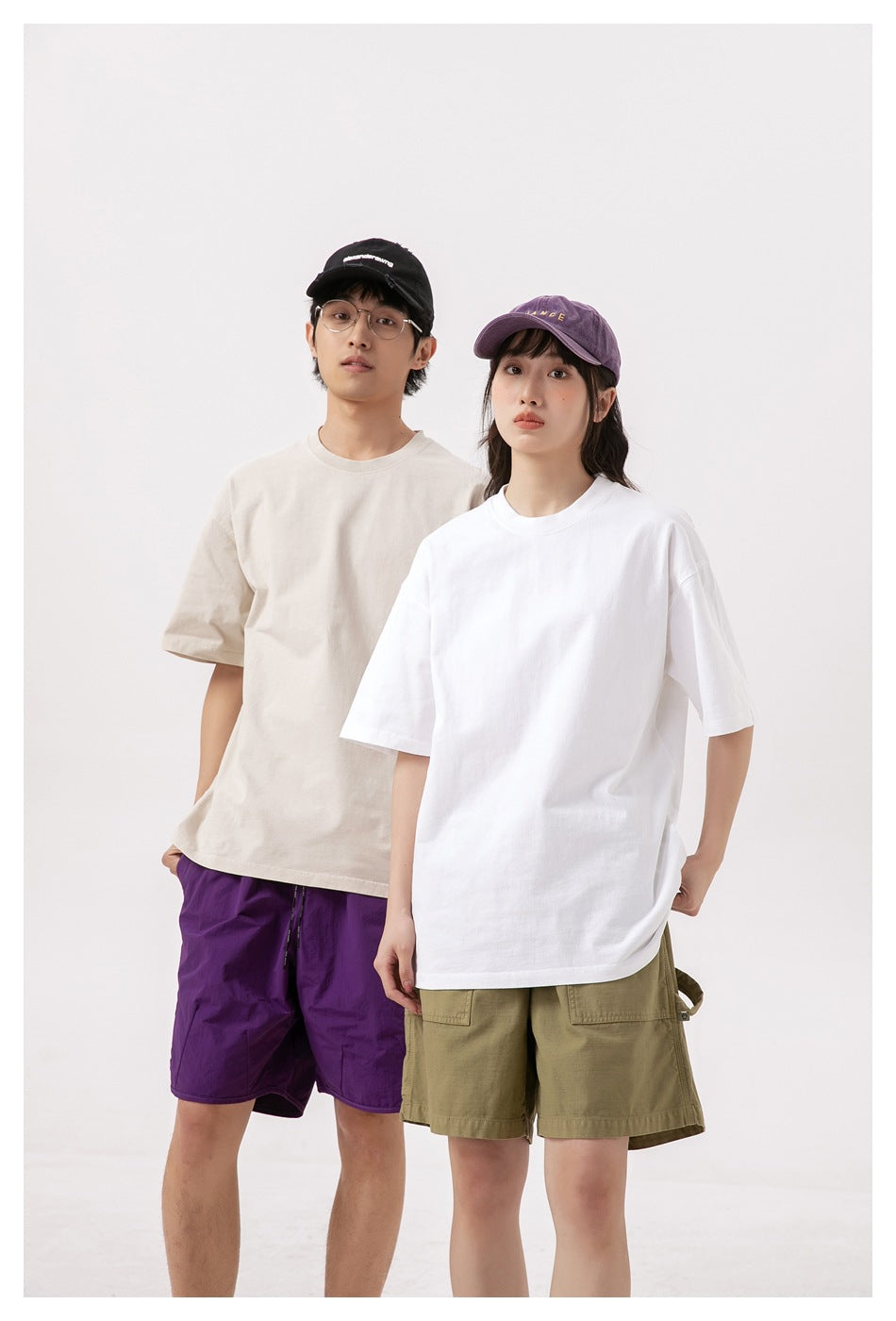 Two models wearing oversized cream and white short-sleeve T-shirts with purple and olive shorts.