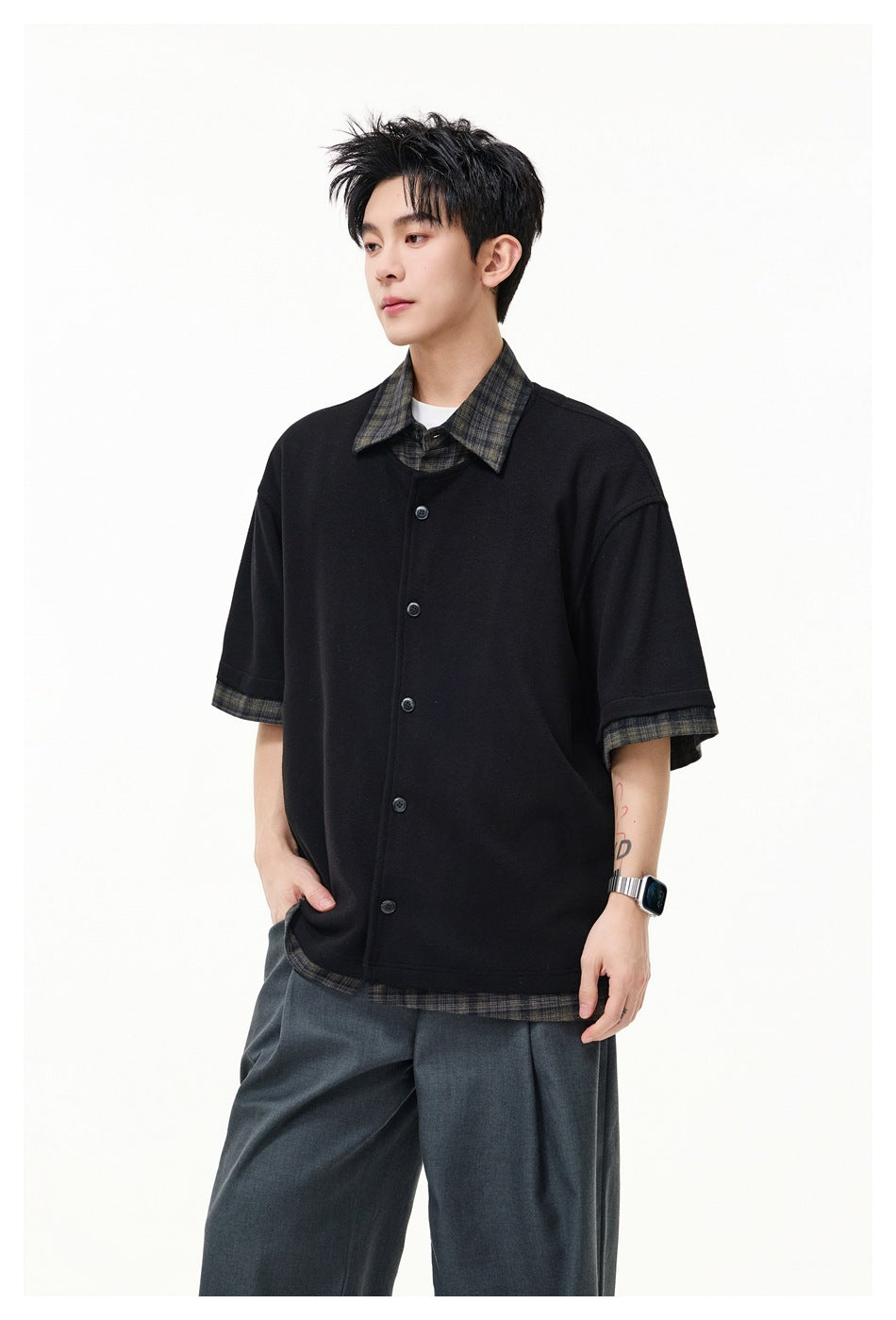 Model wearing black short-sleeve button-front top with plaid collar, cuffs and hem over gray trousers