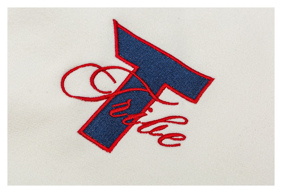Close-up of red and navy embroidery on ivory fabric, with a large angular emblem and script lettering.