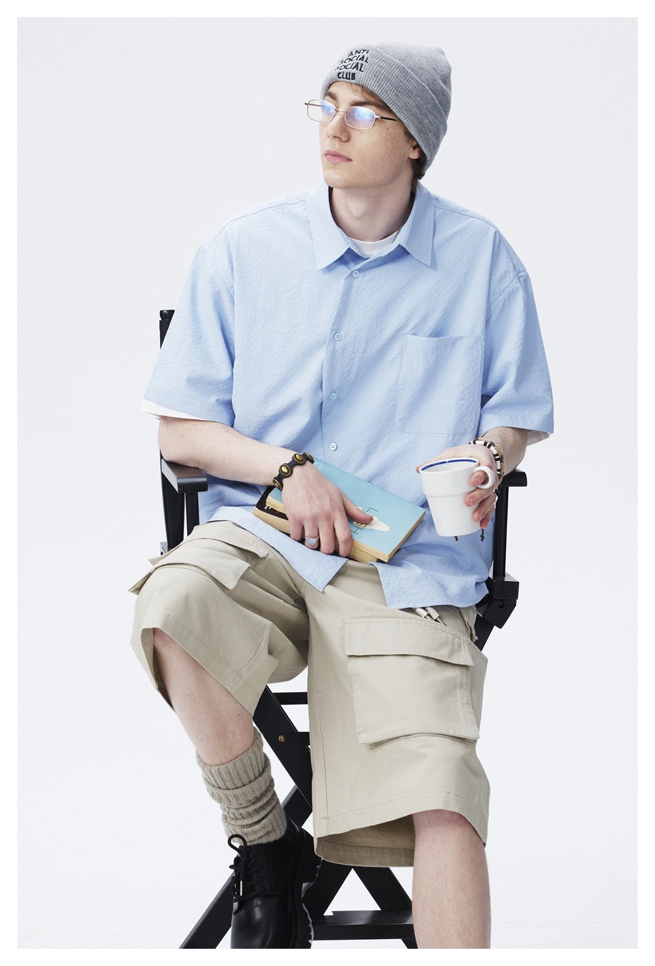 Seated model wearing a light blue short-sleeve button-up shirt with a chest pocket, shown from the front.