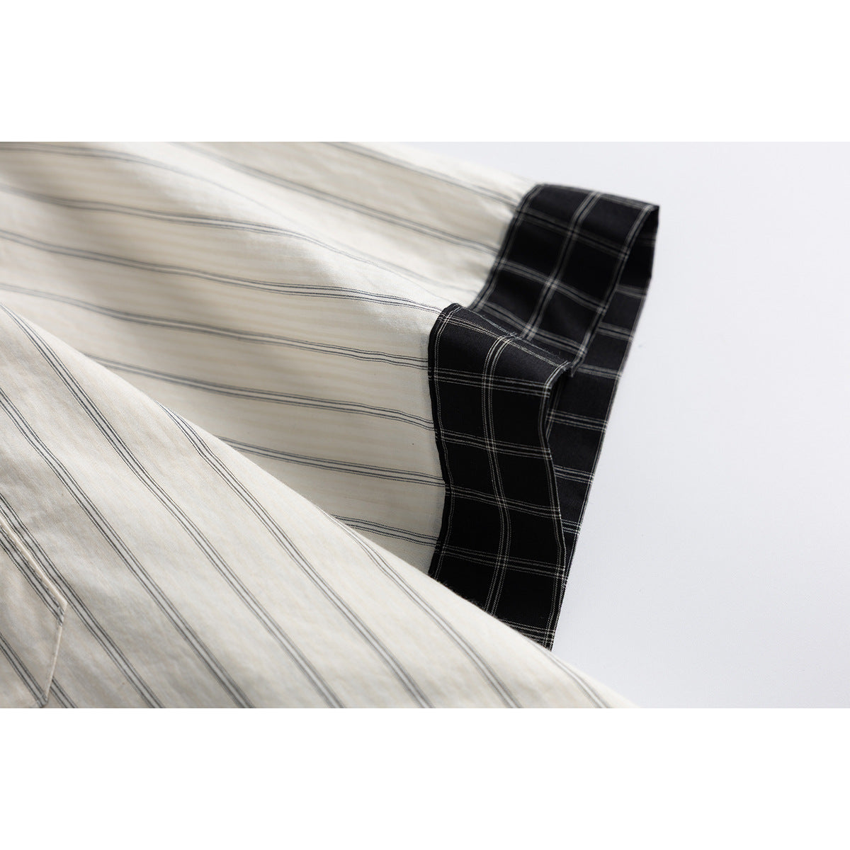 Close-up of a cream striped shirt sleeve with a contrasting black plaid cuff.