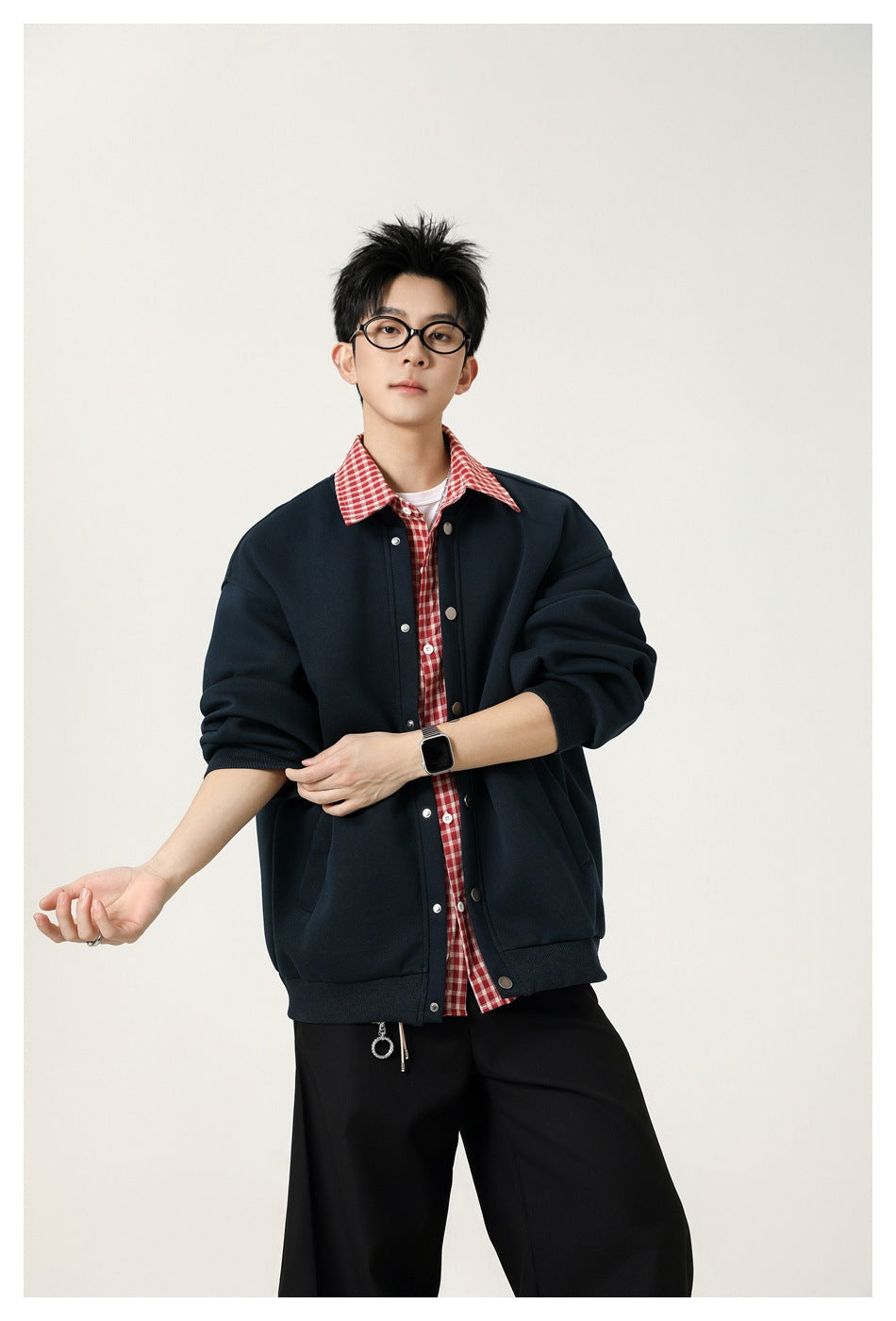 Model wearing an oversized dark navy snap-front jacket over a red checked shirt and black trousers.