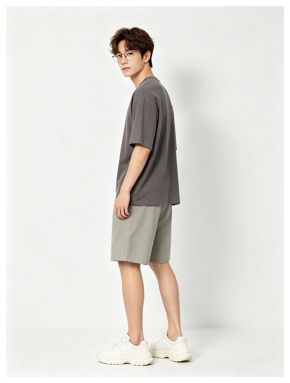 Side view of a man in a gray T-shirt, khaki knee-length shorts and white sneakers