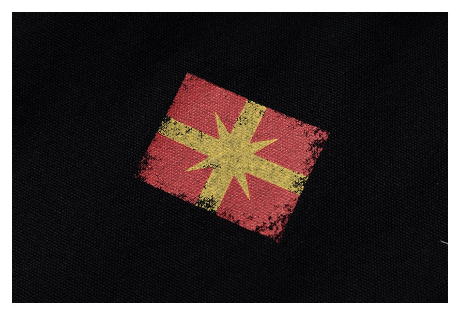 Close-up of a distressed red and yellow starburst graphic printed on black textured fabric.