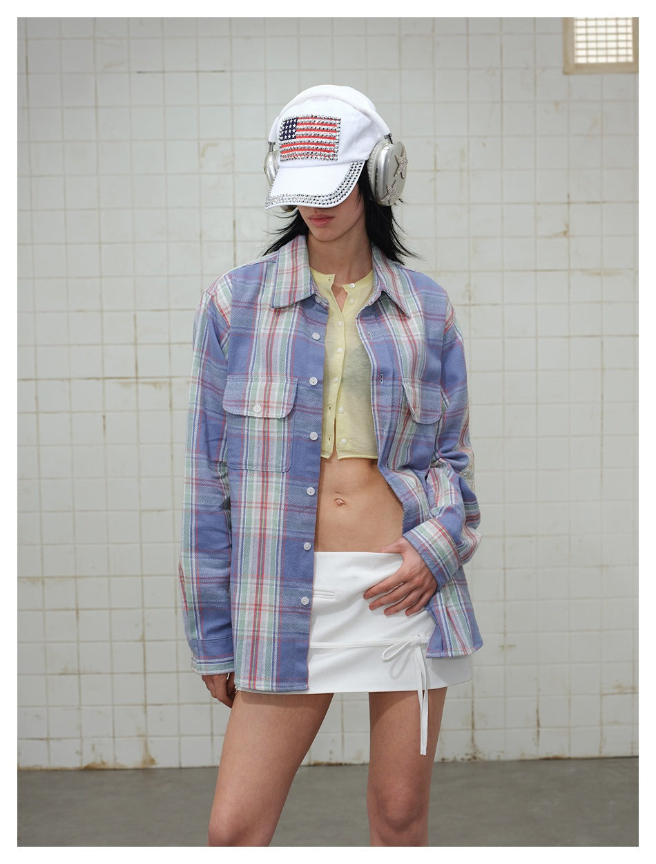 Model wearing an oversized blue plaid button-up shirt over a pale yellow cropped top and white drawstring skirt.