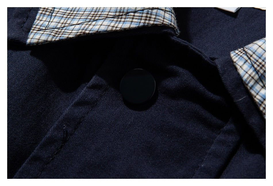 Close-up of a large black snap on the navy jacket, framed by beige-and-blue plaid collar lining.