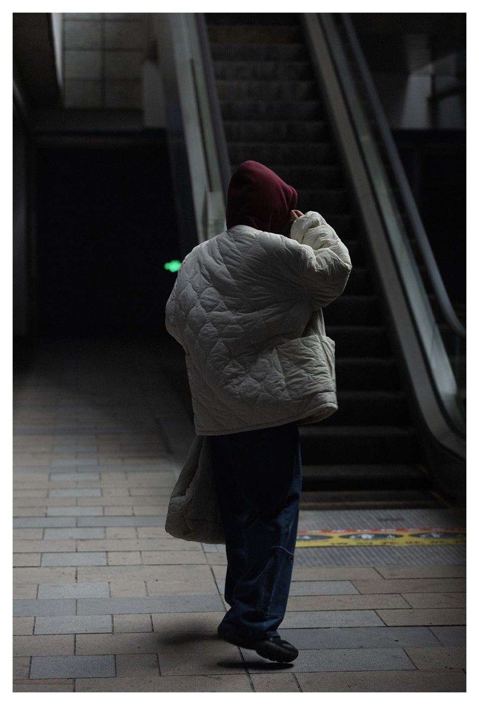 Rear view of a person wearing an off-white quilted jacket over a burgundy hood and dark trousers.