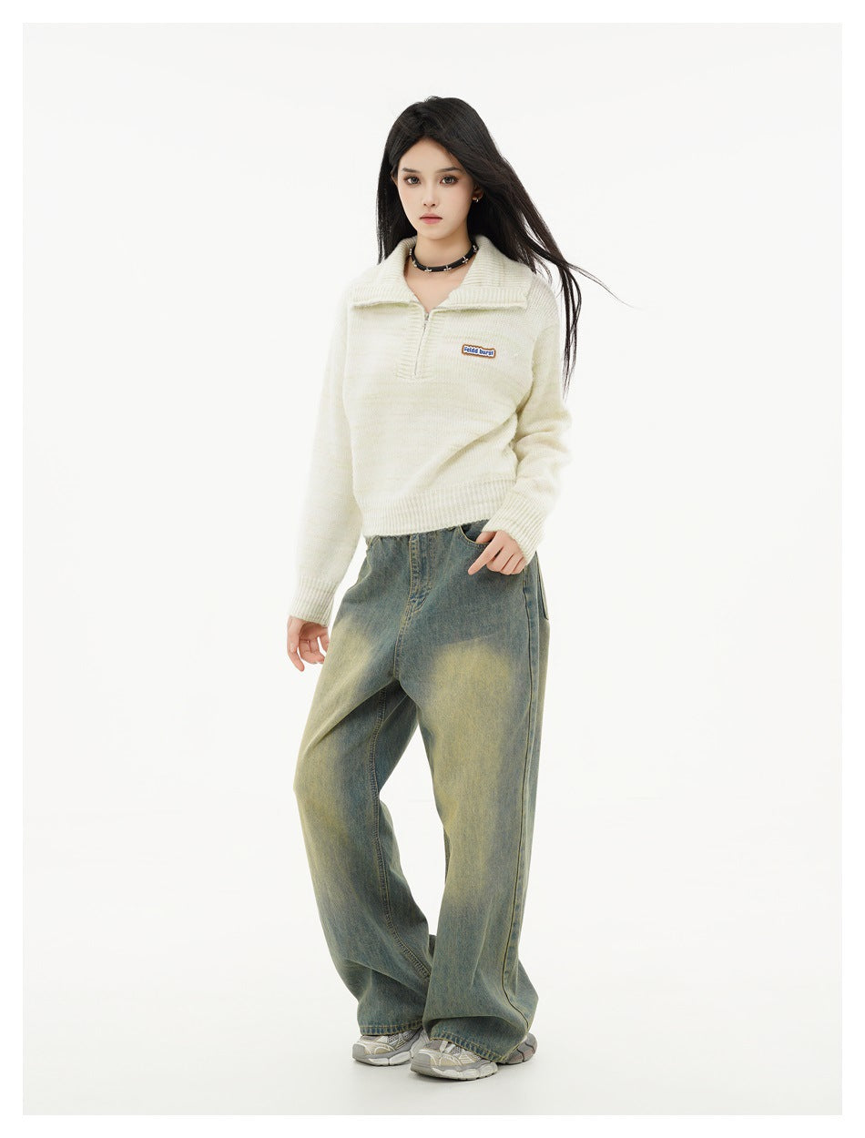 Three-quarter view of a model wearing an ivory knit quarter-zip sweater with loose faded jeans.