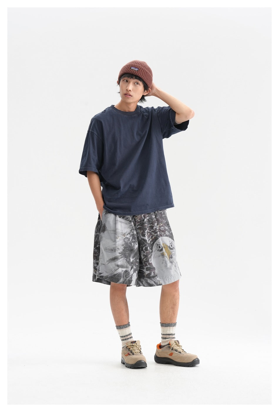 Model in a loose navy T-shirt and gray eagle-print shorts, posing with one hand behind his head.