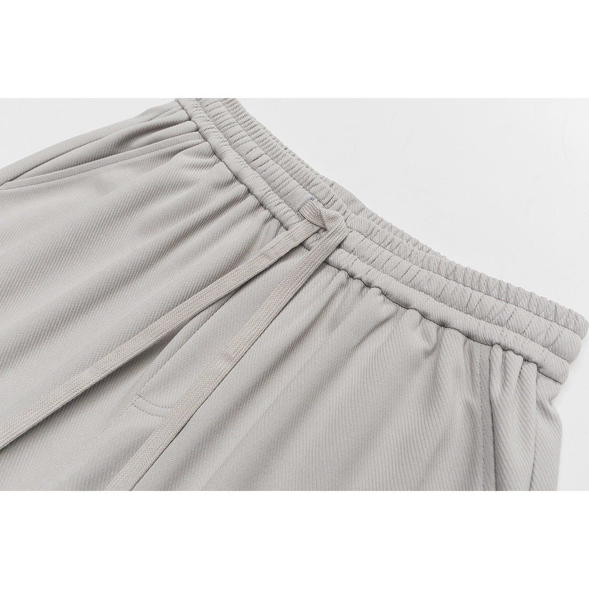 Close-up of light gray shorts with an elastic waistband, drawstring, and gathered fabric.