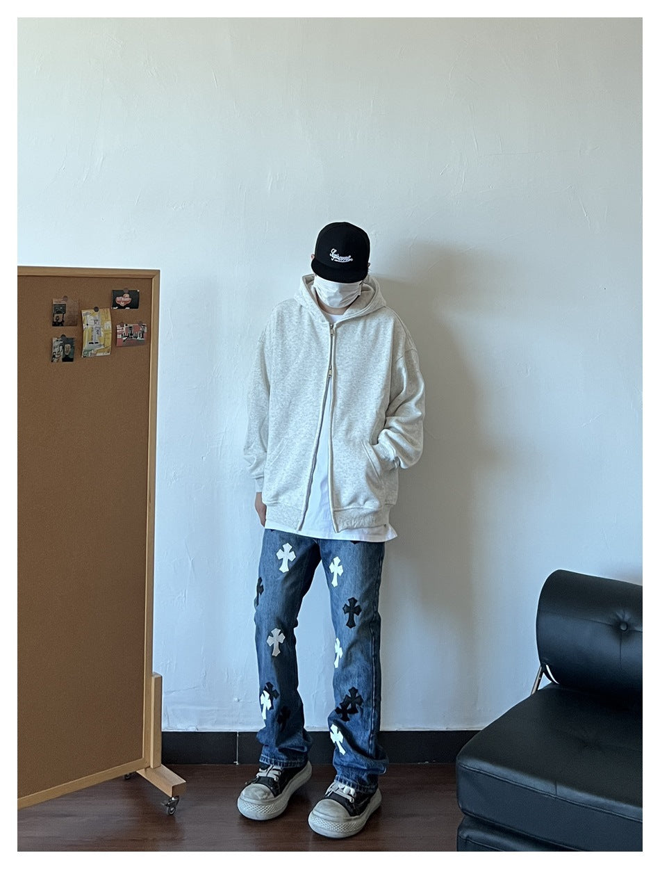 Person wearing an open heather white-gray zip hoodie over a white tee with printed jeans, standing against a white wall