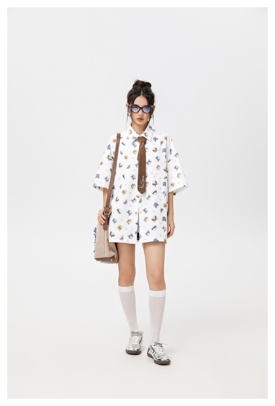 Model wearing the white cat print short-sleeve shirt buttoned with a brown tie, sunglasses, knee socks and a shoulder bag