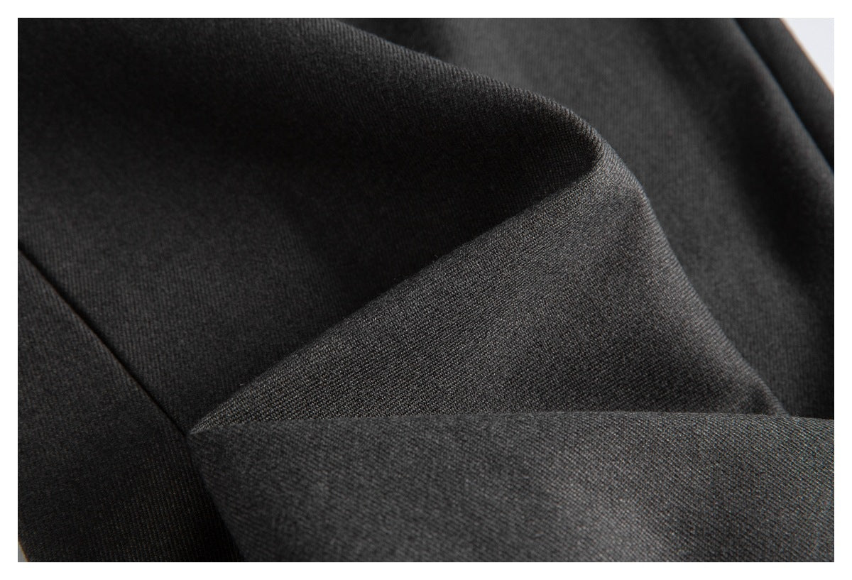Macro view of dark charcoal garment fabric with overlapping folds and a stitched seam.