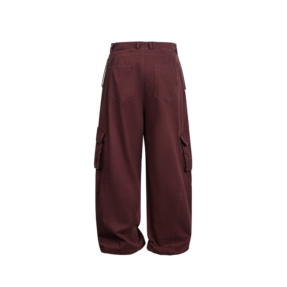 Back view of loose burgundy cargo trousers with two rear patch pockets and flap thigh pockets.