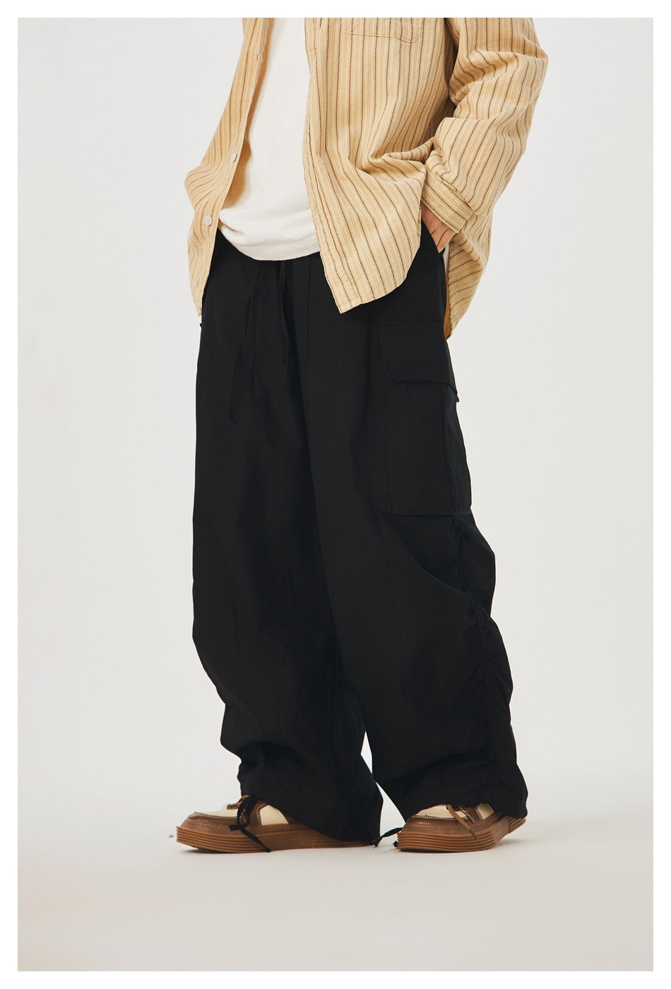 Model wearing loose black cargo pants with a large side pocket, gathered hems, and drawcords.