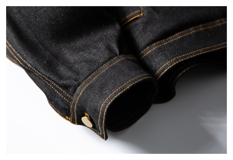Close-up of a black denim jacket cuff with a brass-toned button and golden-brown stitching.