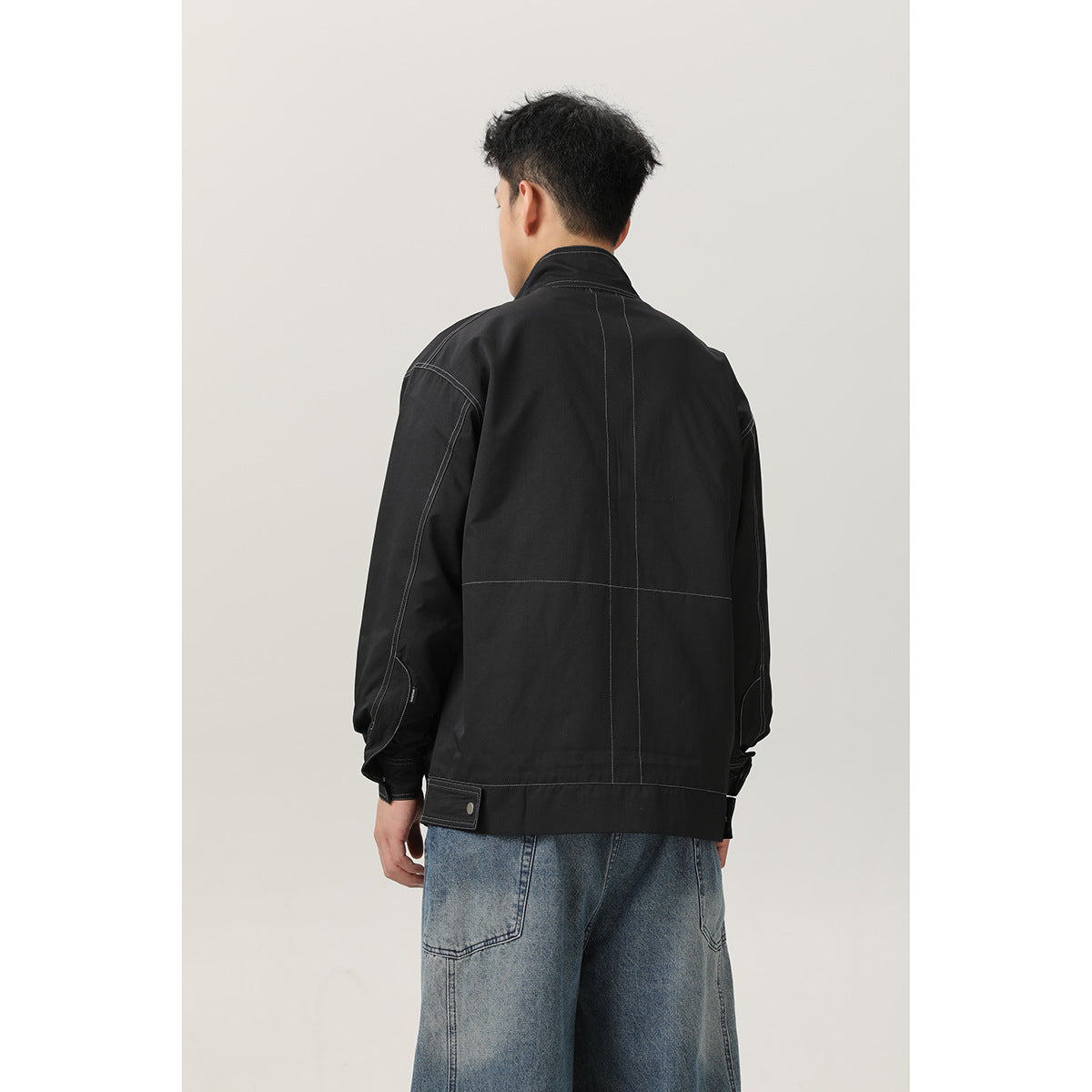Back view of a model wearing a black jacket with contrast stitching and an adjustable hem tab.