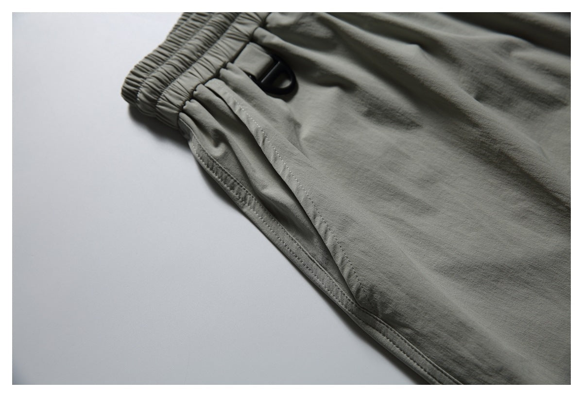 Close-up of the gray-green shorts' gathered elastic waistband, side seam, and small black loop.