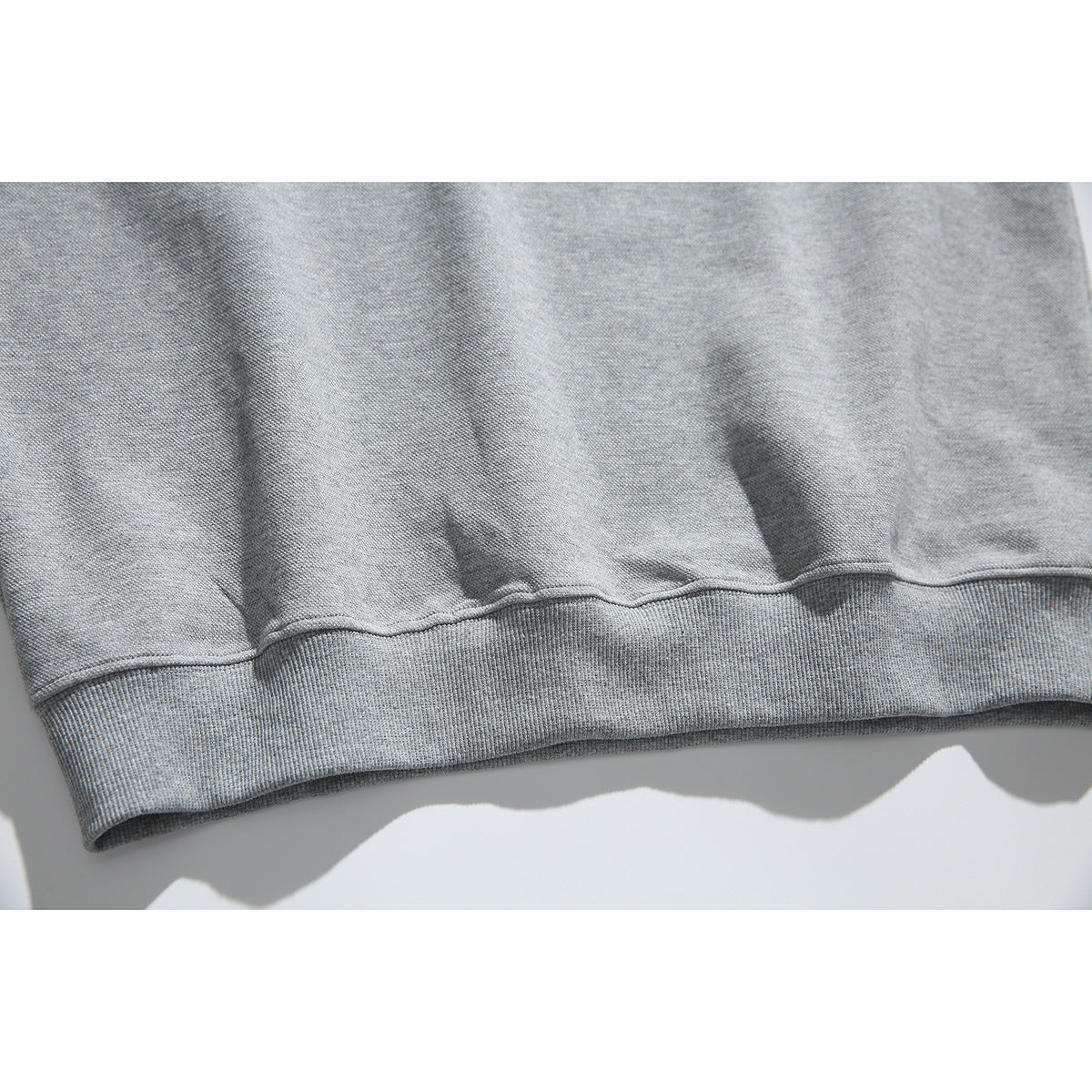 Close-up of the ribbed hem and stitching on a heather gray pullover.