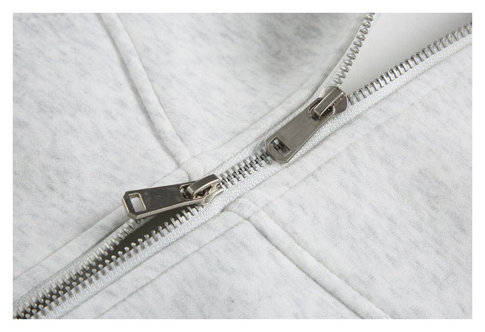 Close-up of a silver zipper with two pulls on light heather gray fabric.