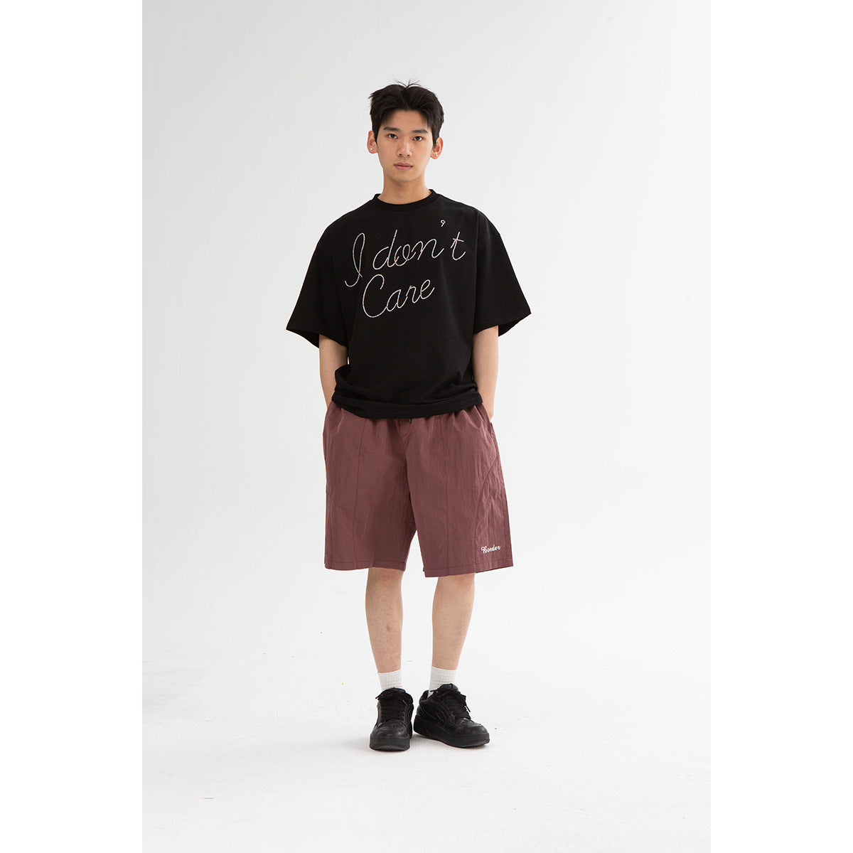 A model wears a black oversized T-shirt with white script and mauve knee-length shorts.