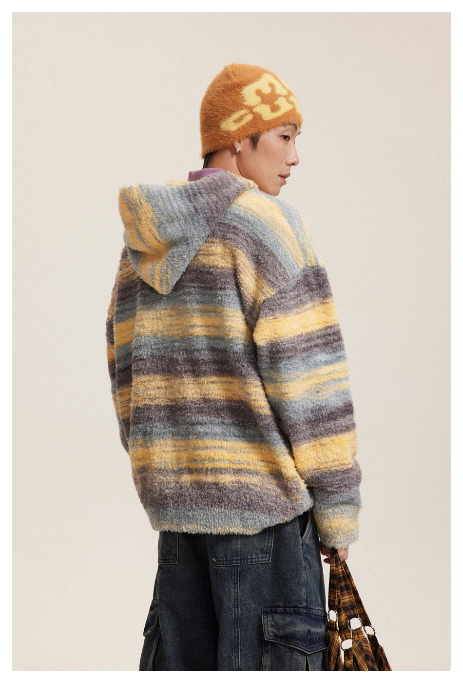 Back view of a model wearing a gray, yellow, and brown striped hooded sweater with the hood down.