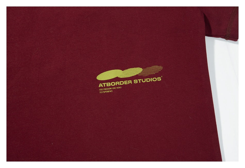 Close-up of a small lime-green graphic and English lettering printed on the burgundy T-shirt.