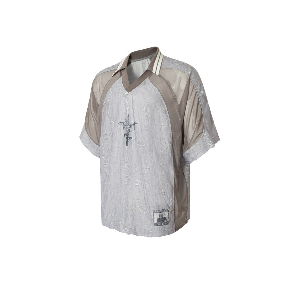 Angled front view of a pale gray textured short-sleeve shirt with taupe panels, striped collar and chest graphic.
