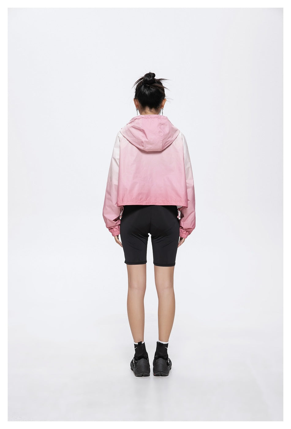 Back view of model wearing a pink gradient cropped hooded jacket with black bike shorts