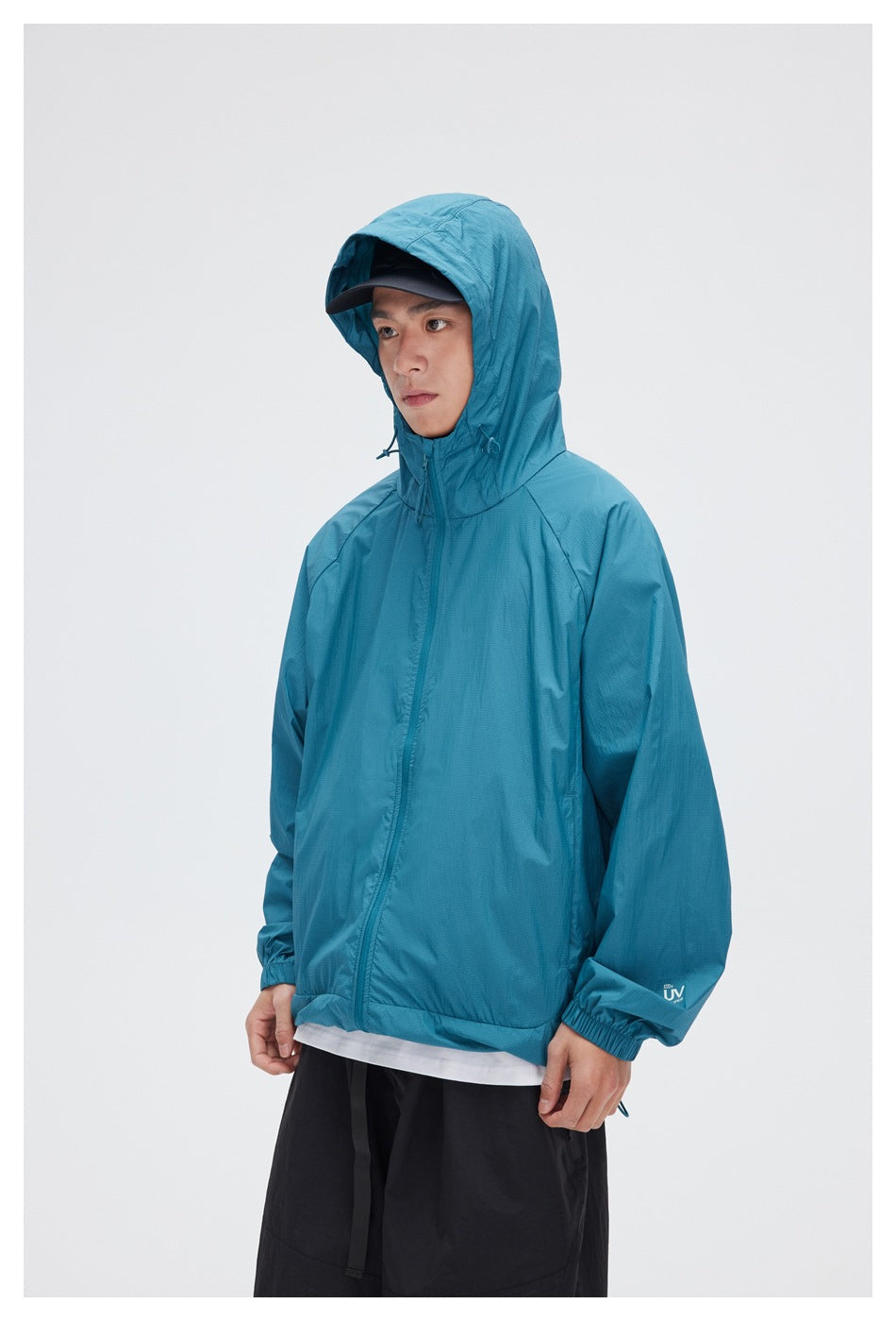 Model wearing a teal hooded zip jacket over a white shirt and black shorts.