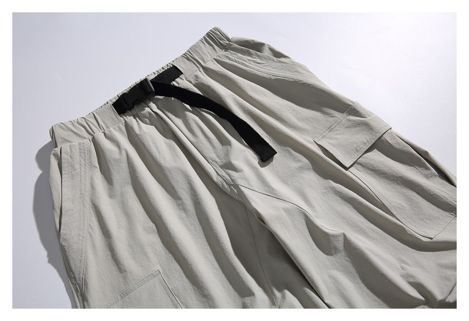 Close-up of light gray cargo joggers showing the elastic waistband, black buckle belt, drawstring, and side pocket.