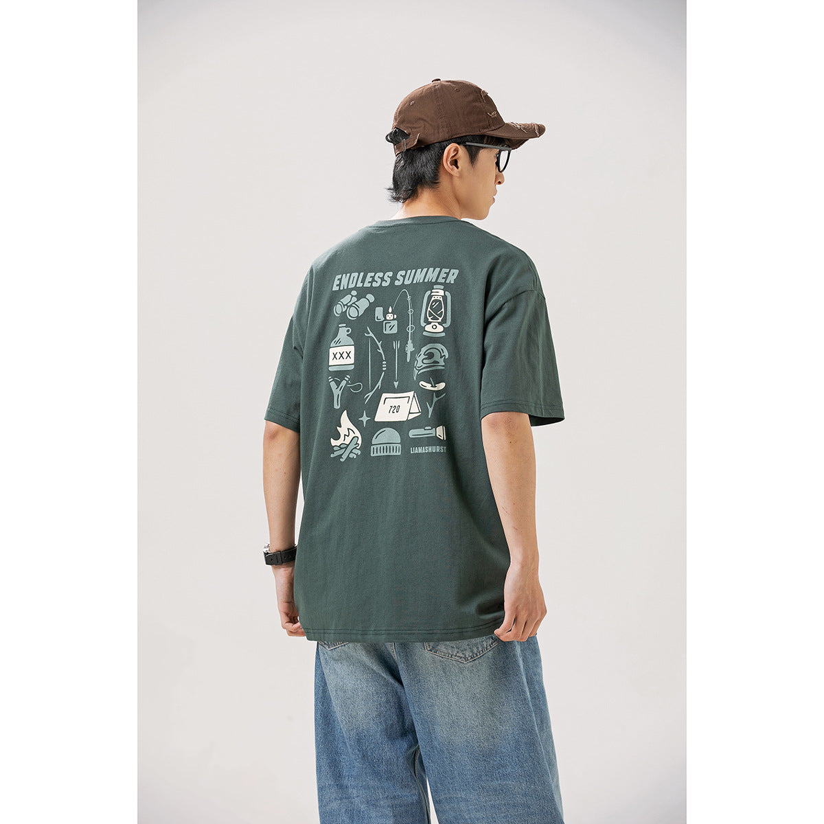 Back view of a model wearing a dark green T-shirt with a large camping-themed graphic and light blue jeans.