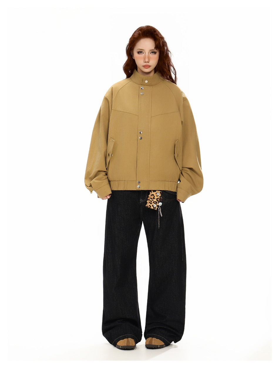 Front view of a model wearing an ochre tan snap-front jacket with a stand collar and angled pockets.
