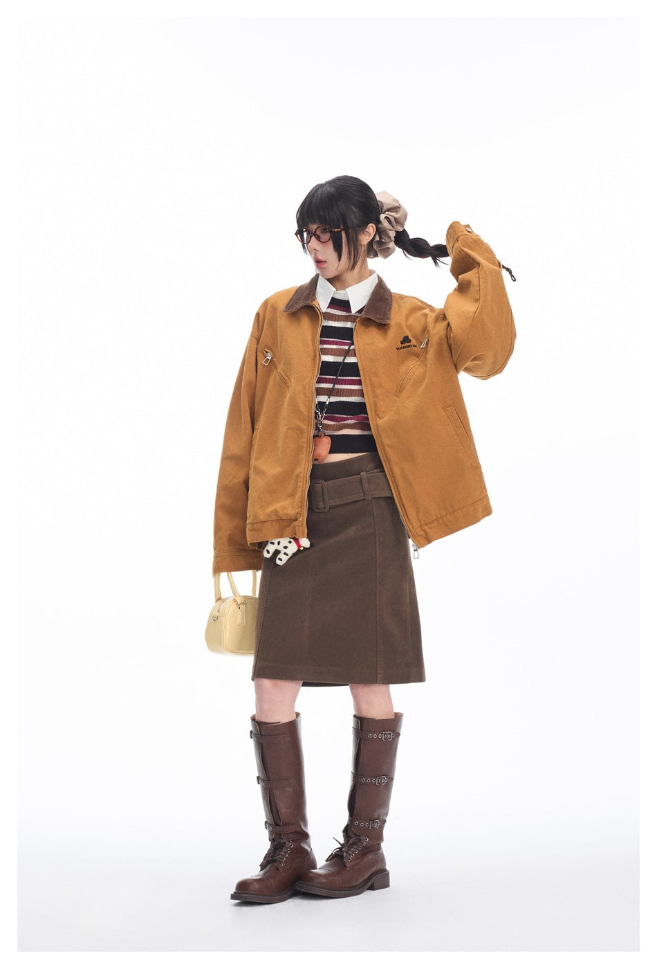 Model wearing the tan-brown zip jacket open over a striped top and brown skirt with tall brown boots, full-length view