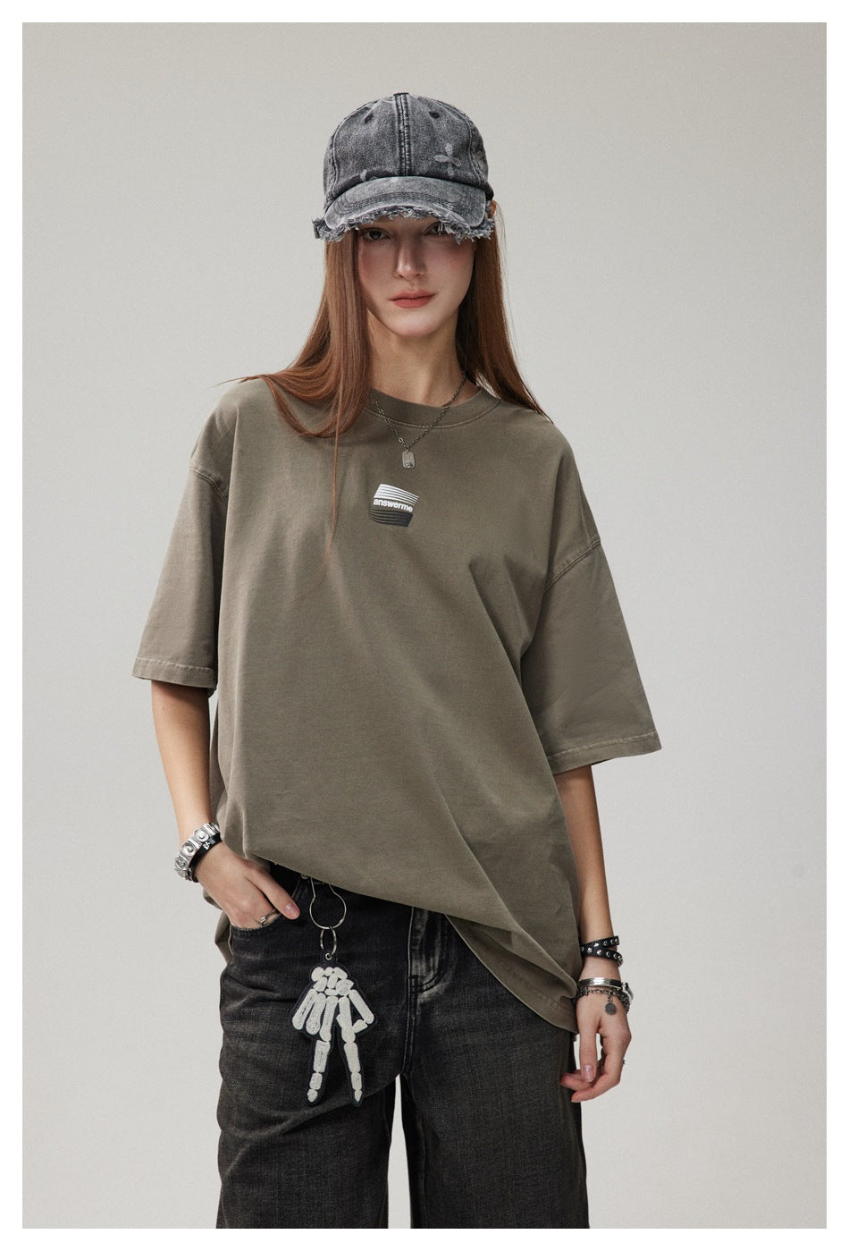 Model wearing an oversized olive taupe T-shirt with a small striped chest graphic, shown from the front.