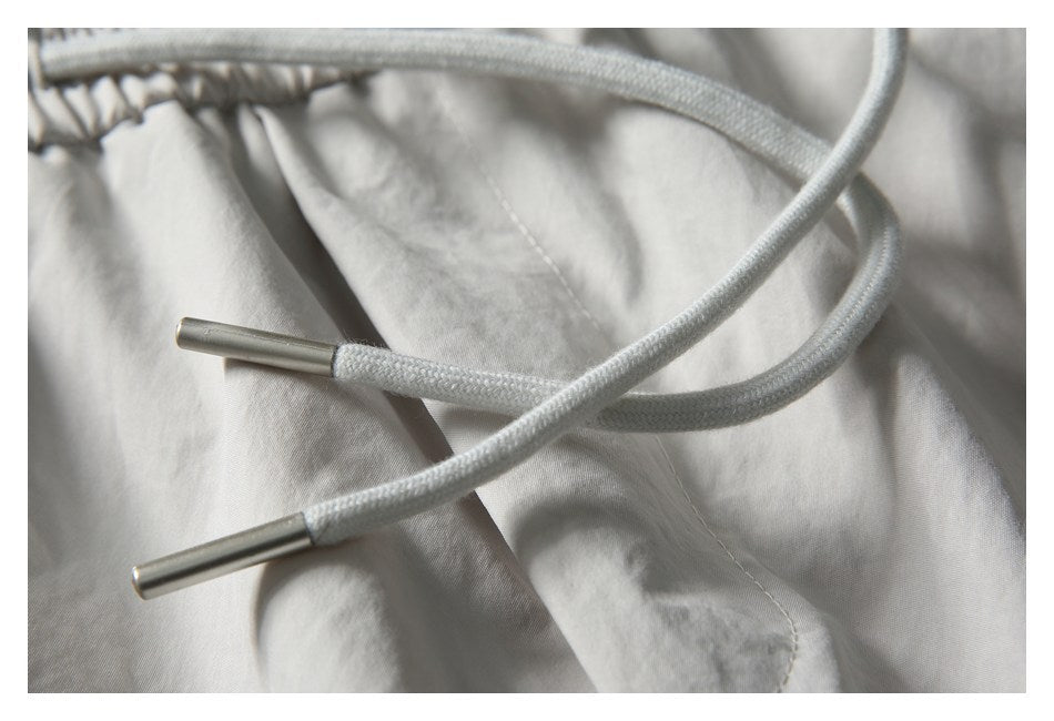 Close-up of white braided drawstrings with metal tips crossing the light gray shorts fabric.