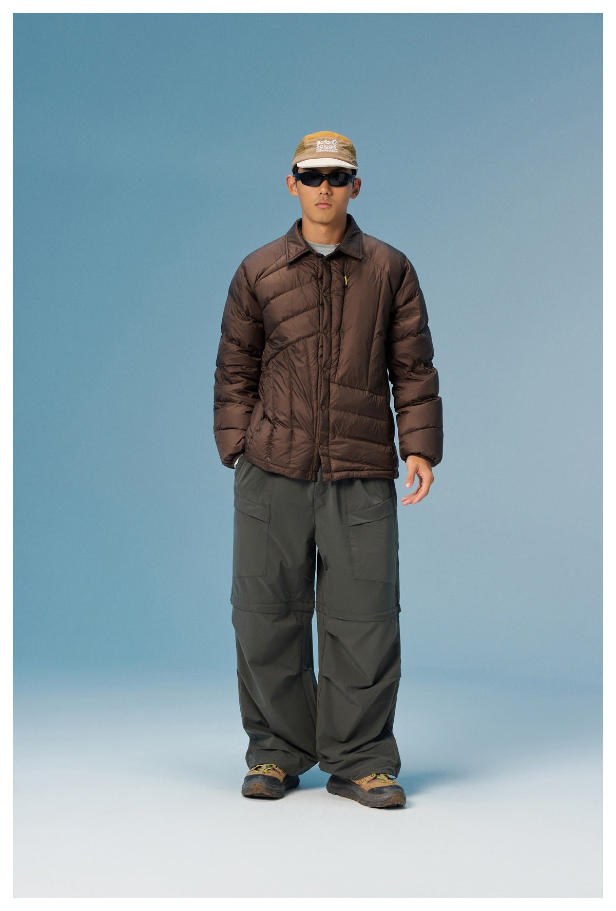 Full-length model wearing a dark brown quilted jacket, loose dark pants, and hiking shoes.