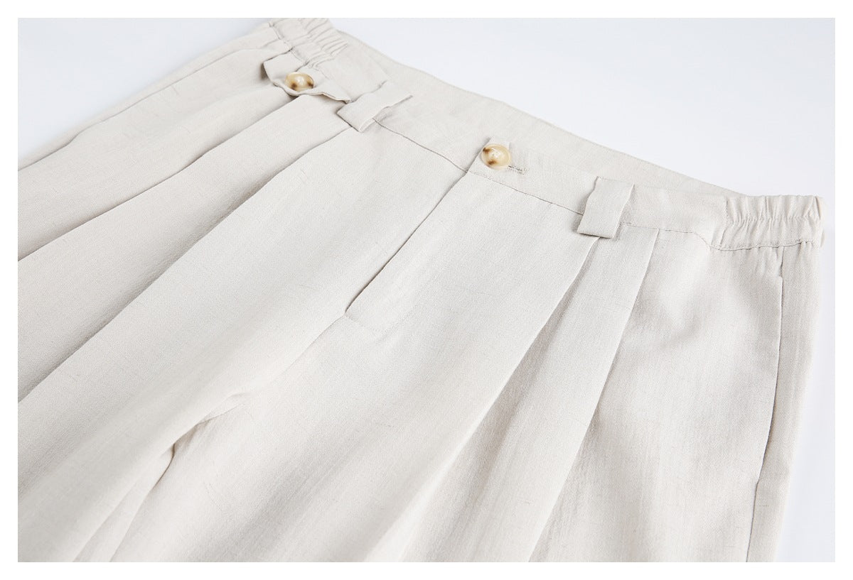 Close-up of ivory trousers showing pleats, tan buttons, belt loops, and an elasticized waistband section.