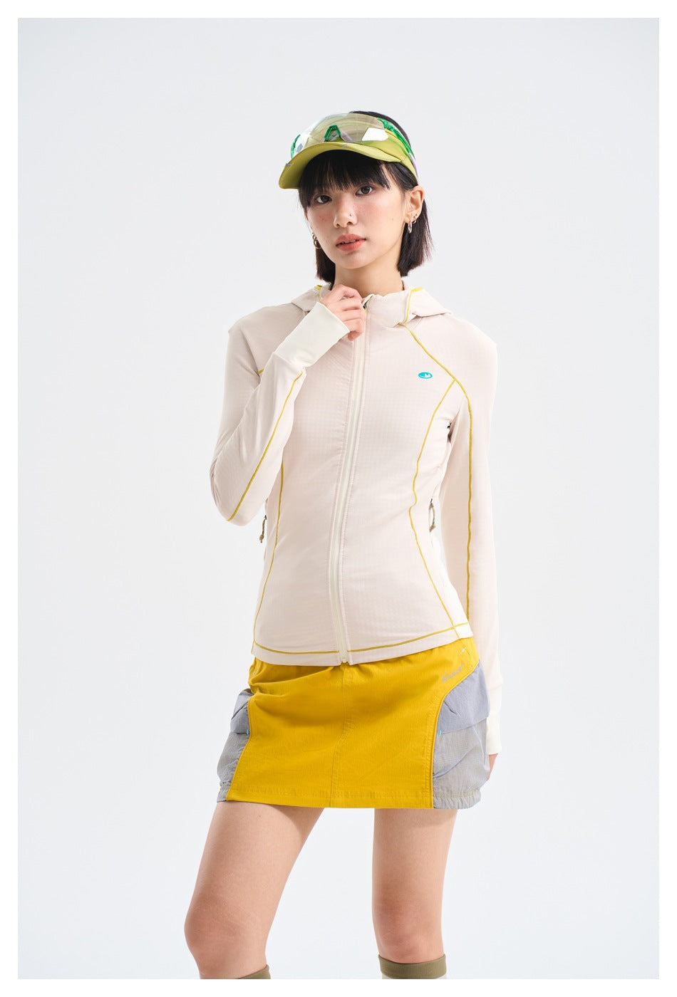 Model wearing an ivory hooded zip jacket with yellow piping and a color-block yellow-and-gray skirt.