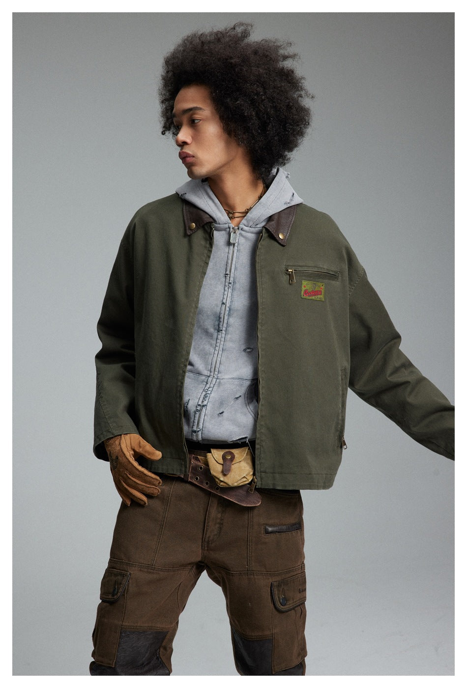 Model wearing an olive jacket with a brown collar and chest zip pocket over a gray hoodie.
