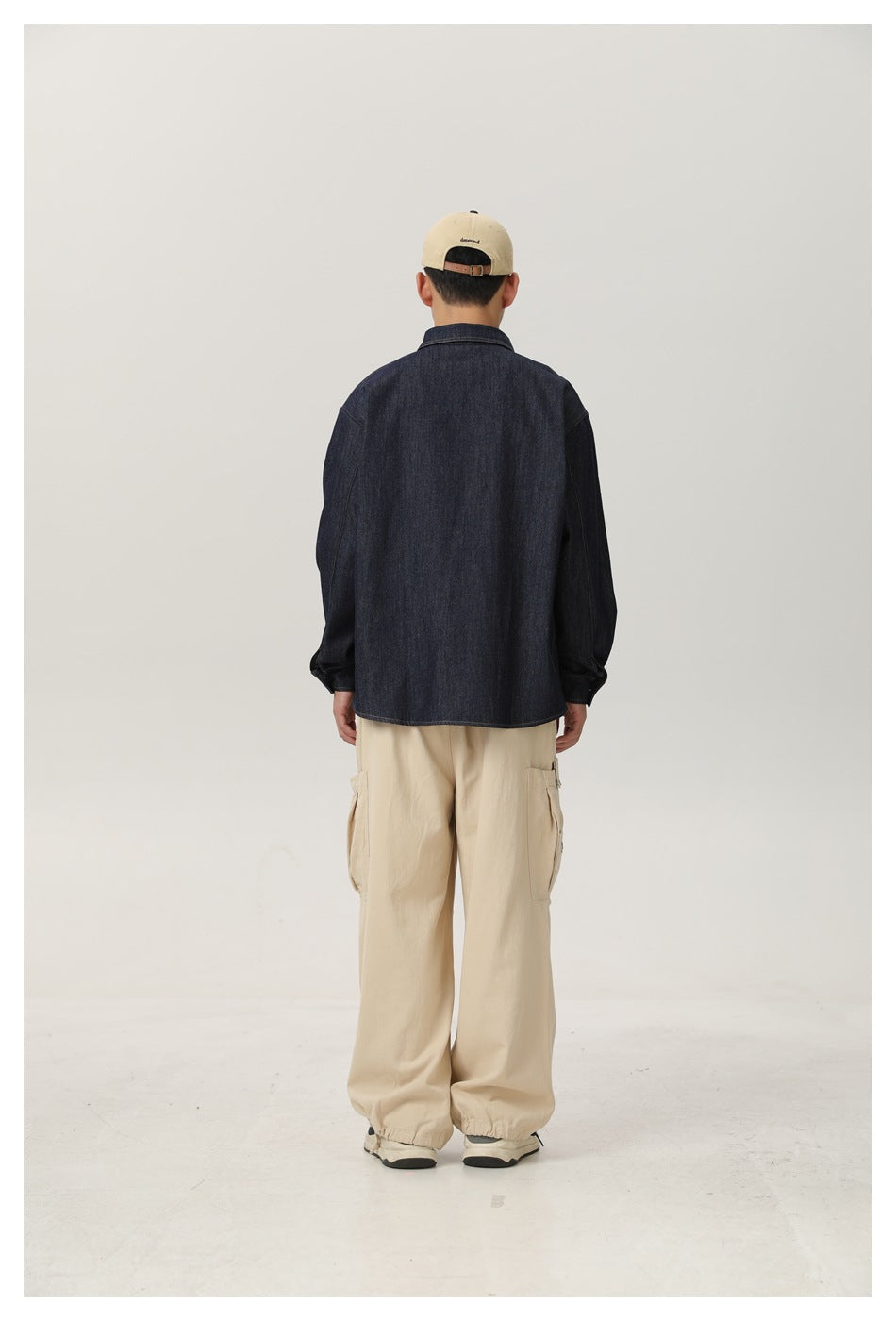 Back view of model wearing a dark denim shirt with beige cargo pants and a cap
